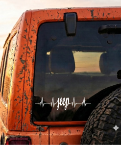 Mud-splattered orange Jeep rear corner with a mounted spare tire and a heartbeat-style Jeep logo on the rear window