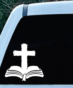 White Christian symbols: a cross over an open Bible against a dark car window backdrop, suggesting a religious decal on a vehicle window.