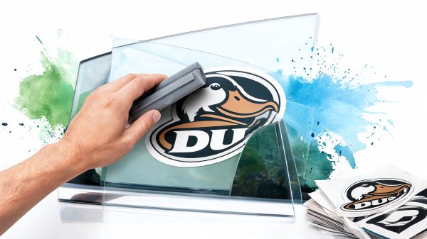 Close-up of a hand applying a sticker featuring a duck logo onto a glass surface, with watercolor splash background.