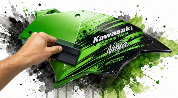 Close-up of a hand polishing a green and black Kawasaki Ninja 400 motorcycle fairing with a sanding block, set against paint-splatter background