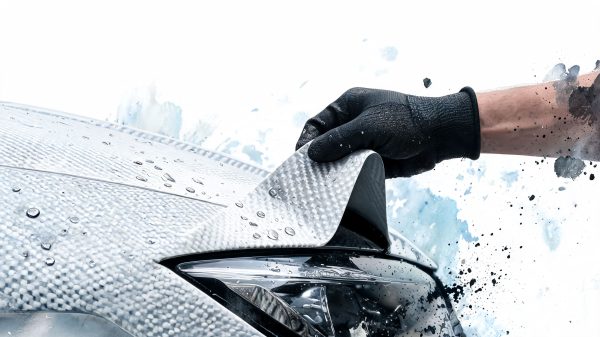 Close-up of a gloved hand pulling a textured car roof panel during washing, with water droplets and splashes around.