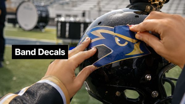 Person applying a blue and gold band decal to a black helmet on a football field; a black label reads 'Band Decals'.