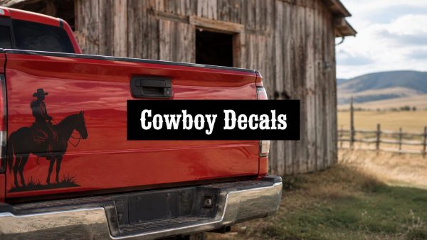 Red pickup tailgate with a black cowboy decals silhouette and bold 'Cowboy Decals' text overlay on the tailgate, rural barn and fields in the background, outdoor scene