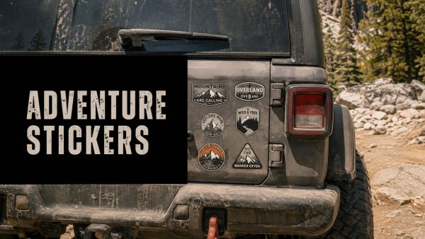 Back of a dusty Jeep with a large black panel reading 'ADVENTURE STICKERS' and several mountain-themed stickers on the right tailgate.