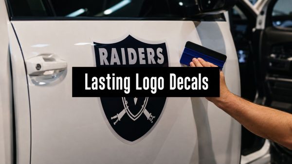 Person uses a blue squeegee to apply a Raiders logo decal to a white car door.